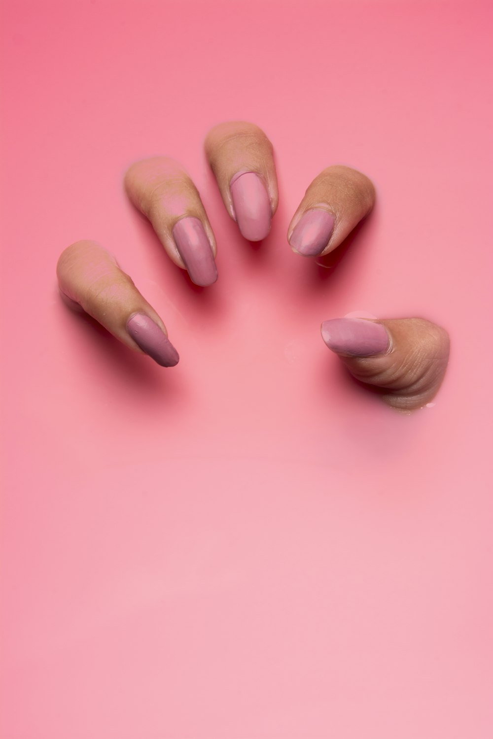 Mano con uñas rosas sobre fondo rosa